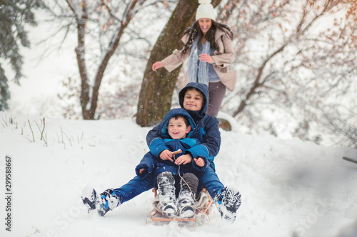 Young mom chasing her cute sons while they are sledding