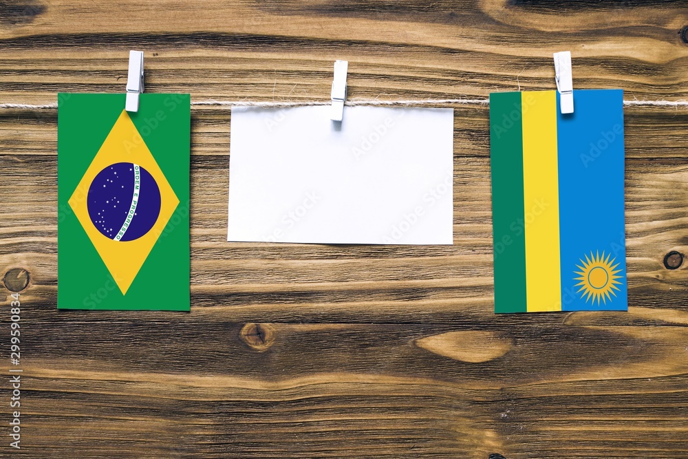 Hanging flags of Brazil and Rwanda attached to rope with clothes pins with copy space on white note paper on wooden background.Diplomatic relations between countries. Hanging flags of Brazil and Rwanda attached to rope with clothes pins with copy space on white note paper on wooden background.Diplomatic relations between countries.