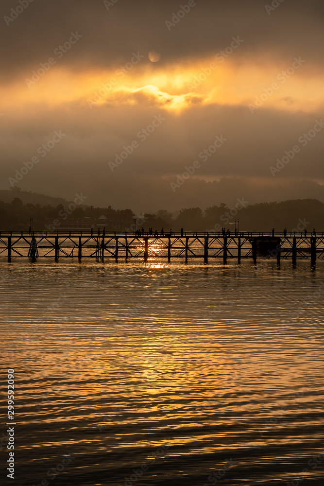 Fototapeta premium Old wooden bridge over the river (Mon Bridge) in sunrise at Sangkhla Buri District, Kanchanaburi, Thailand.