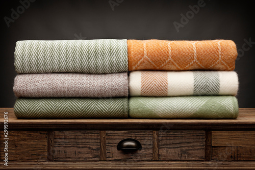 6 luxury throws, folded up and shot on a wooden sideboard,  with a grey background