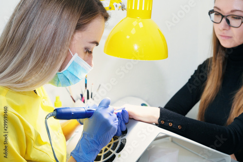 Nail care. Manicure in the salon. The master manicures the girl, beauty and health. Manicure process. Master in mask and gloves. Using the apparatus for manicure. Equipment in a beauty salon.