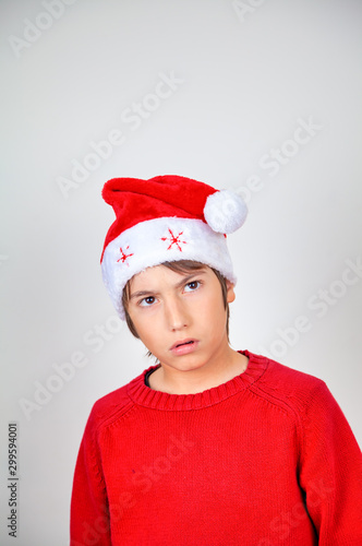 Happy young boy with Christmas hat at home making worried face, isolated on white background