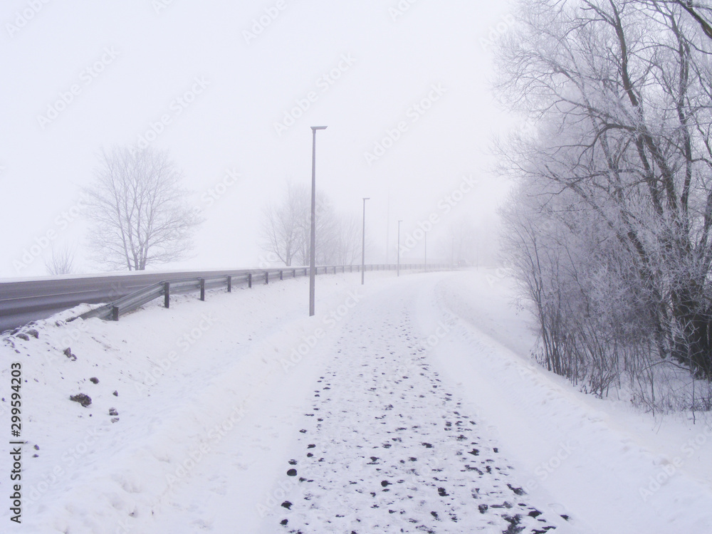 Misty morning in winter with a little bit of snow. Landscape with a roadside and pedestrian footprints on the pathway. Misty morning in winter with a little bit of snow. Landscape with a roadside and pedestrian footprints on the pathway.