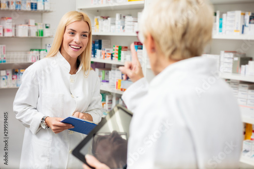 Smiling happy young and mature female pharmacists working behind the counters in a pharmacy, talking and discussing. Healthcare and medicine concept.