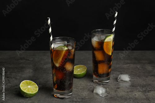 Refreshing soda drinks with straws on grey table against black background