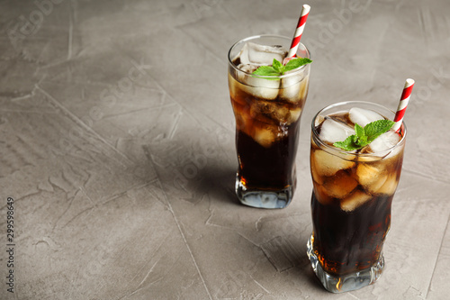 Glasses of refreshing soda drink with ice cubes and straws on grey table, space for text