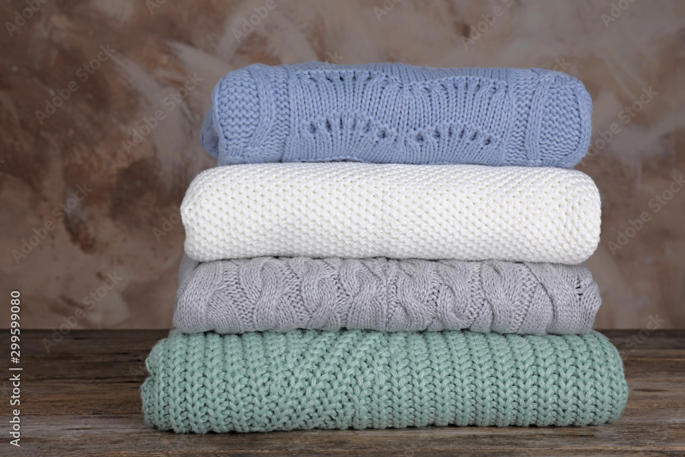 Stack of folded knitted sweaters on wooden table against brown background