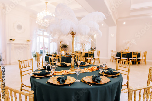 Table decoration with flowers in white colors. Elegant dining table in green-golden color. Indoors wedding. Devices and chairs in golden colors. Beautiful table setting, tablecloth green.