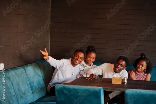Happy african friends sitting and chatting in cafe. Group of black peoples meeting in restaurant and calling waiter.
