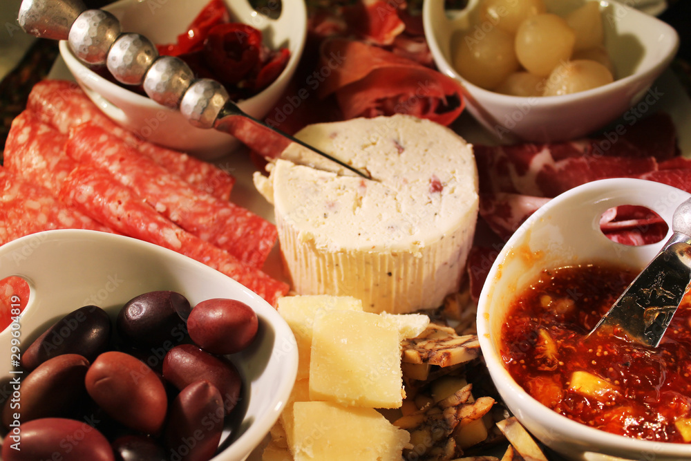 Close-up of a Charcuterie board. Kalamata olives, genoa salami, roasted red peppers, prosciutto, pickled onions, capicola, savory fig jam, stout aged cheddar, grana padano cheese, goat cheese.