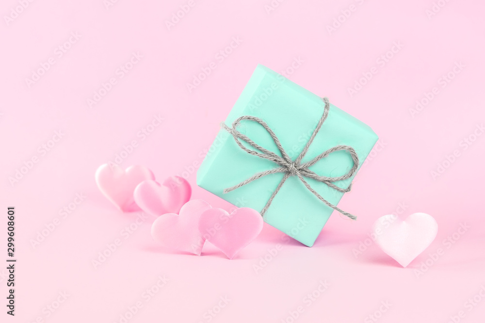 Gift box of blue color decorated with a string of twine on a pink background among pink silk hearts. Holiday concept. Place for text.