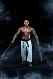 Shirtless man samurai with Japanese sword. Karate fighter on black background with smoke. Handsome and fit man sportsmen bodybuilder physique and athlete. Men's sport motivation.