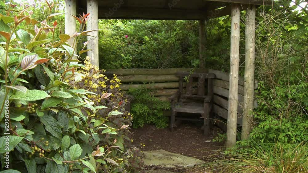 Wide shot of a shelter made of logs in a garden, with small chairs inside Wide shot of a shelter made of logs in a garden, with small chairs inside