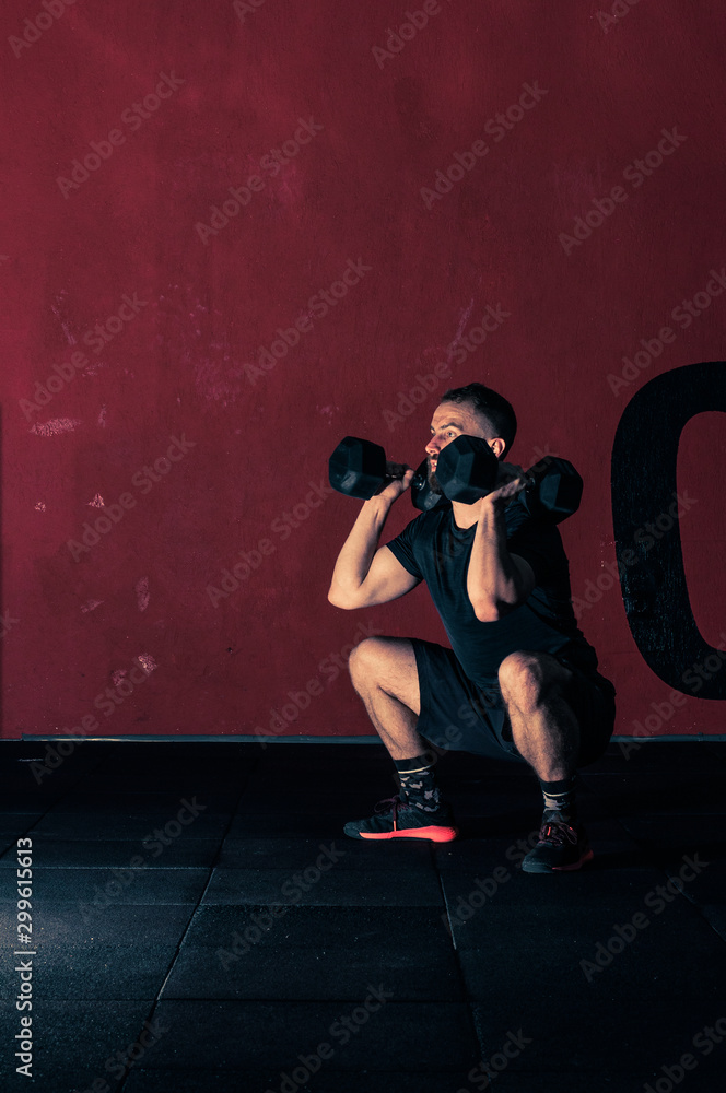 young athlete performs front squats with dumbbells in the gym for functional training, photo in a dark key, the concept of sports and motivation
