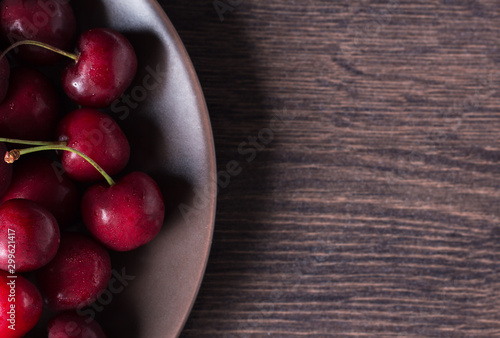 Cherries on a brown plate. Food with copyspace on a wooden table. Berries, snacks, healthy food. Vegan, vegetarian, diabetic, fruit.