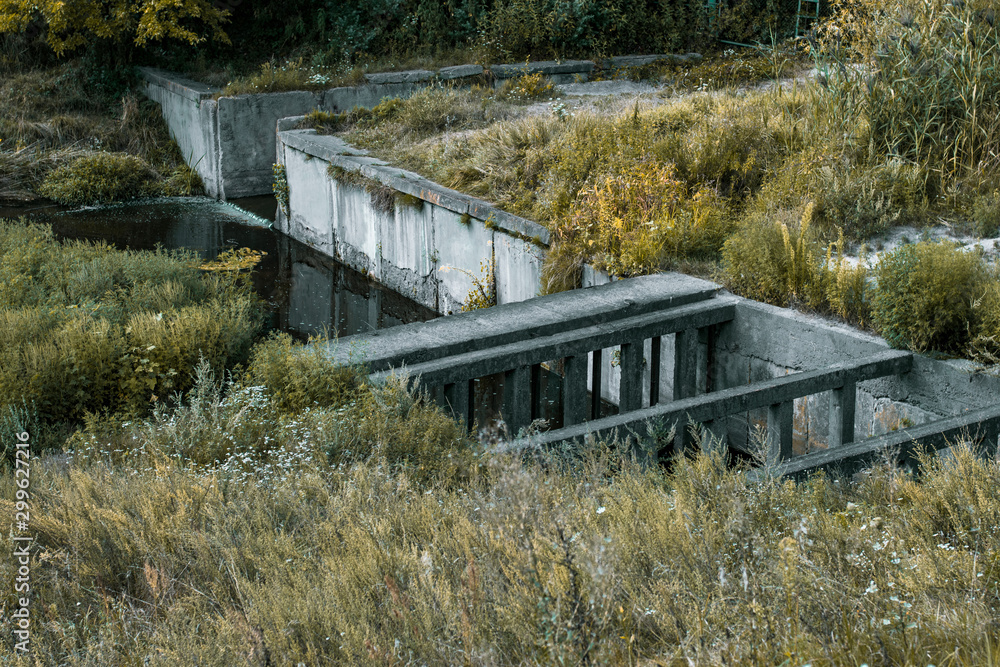 A small concrete bridge across the canal with the streaming waste. Waste flow under the concrete structure of the drain manifold A small concrete bridge across the canal with the streaming waste. Waste flow under the concrete structure of the drain manifold
