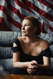 Stylish woman sitting on a sofa against of the American flag.