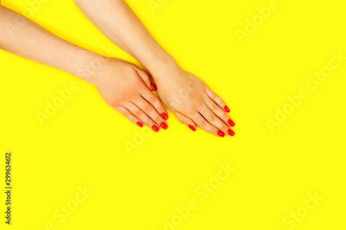 Stylish trendy female manicure. Beautiful young woman s hands on yellow background. Red nails. Flat lay.