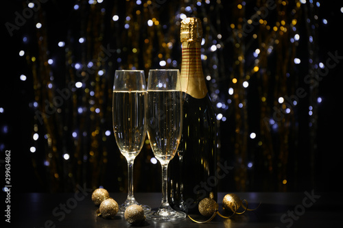 Christmas baubles, champagne glasses and bottle on blurred background, copy space
