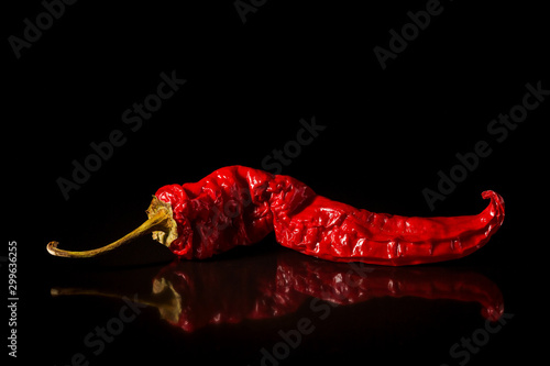 Single red dried banana pepper on a black background with a reflection