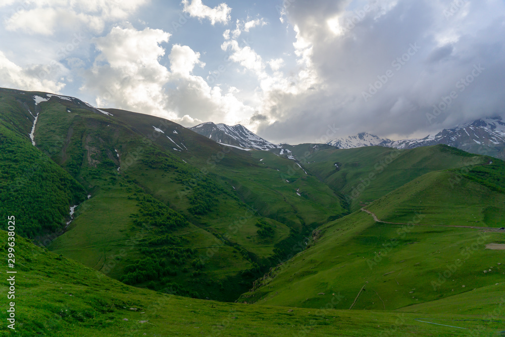 Landscape mountain view peaks in snow and green hills, deep blue sky and huge white clouds background, Caucasian mountains, Kazbek mountain Landscape mountain view peaks in snow and green hills, deep blue sky and huge white clouds background, Caucasian mountains, Kazbek mountain
