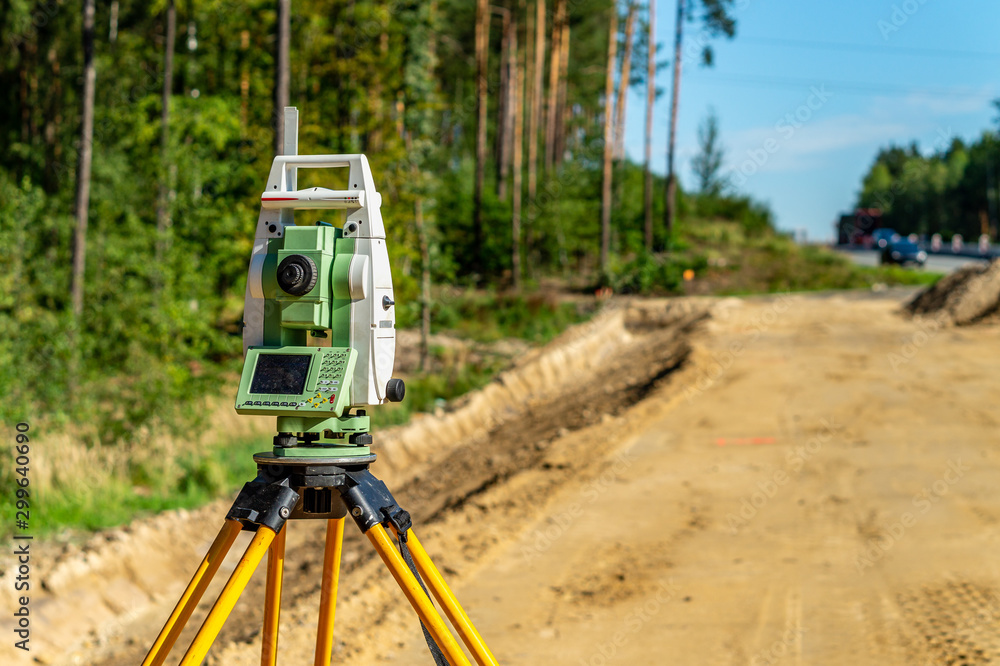 Surveyor engineer with equipment (theodolite or total positioning station) on the construction site of the road or building with construction machinery background Surveyor engineer with equipment (theodolite or total positioning station) on the construction site of the road or building with construction machinery background