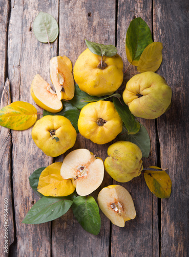 Photos Ripe large quince fruit and slice   with green foliage in late autumn on brown wooden table