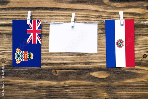 Hanging flags of Cayman Islands and Paraguay attached to rope with clothes pins with copy space on white note paper on wooden background.Diplomatic relations between countries. photo