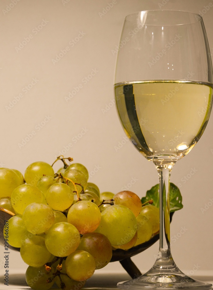  Glass with white wine and a vase with grapes close-up on a light background