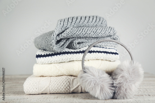 Folded knitted sweaters with fluffy earmuffs and scarf on grey background