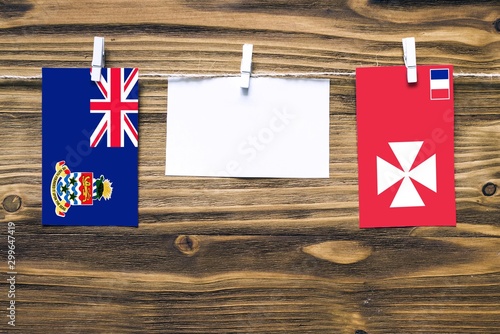 Hanging flags of Cayman Islands and Wallis And Futuna attached to rope with clothes pins with copy space on white note paper on wooden background.Diplomatic relations between countries. photo