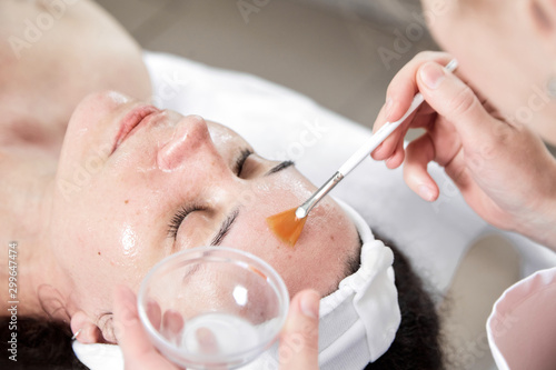 Facial peeling, skin treatment. A dermatologist applies of phytic acid with a white fan brush on female face. A caucasian woman in cosmetic clinic. Cosmetology, facial skin care. Girl in beauty salon photo