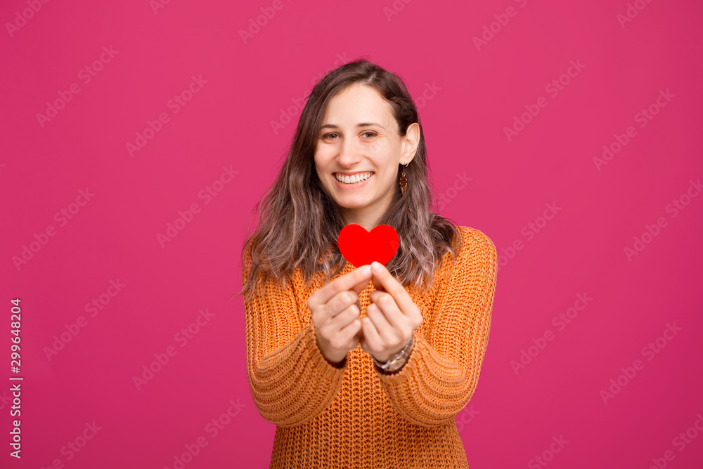 Portrait of charming young woman smiling and looking at the camera and holding paper heart shape Portrait of charming young woman smiling and looking at the camera and holding paper heart shape