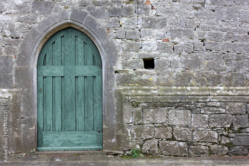 Turquoise colored wooden back door on an exterior wall of a gothic church © Mauro Carli