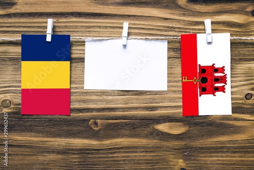 Hanging flags of Chad and Gibraltar attached to rope with clothes pins with copy space on white note paper on wooden background.Diplomatic relations between countries. photo