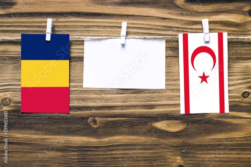 Hanging flags of Chad and Northern Cyprus attached to rope with clothes pins with copy space on white note paper on wooden background.Diplomatic relations between countries. photo