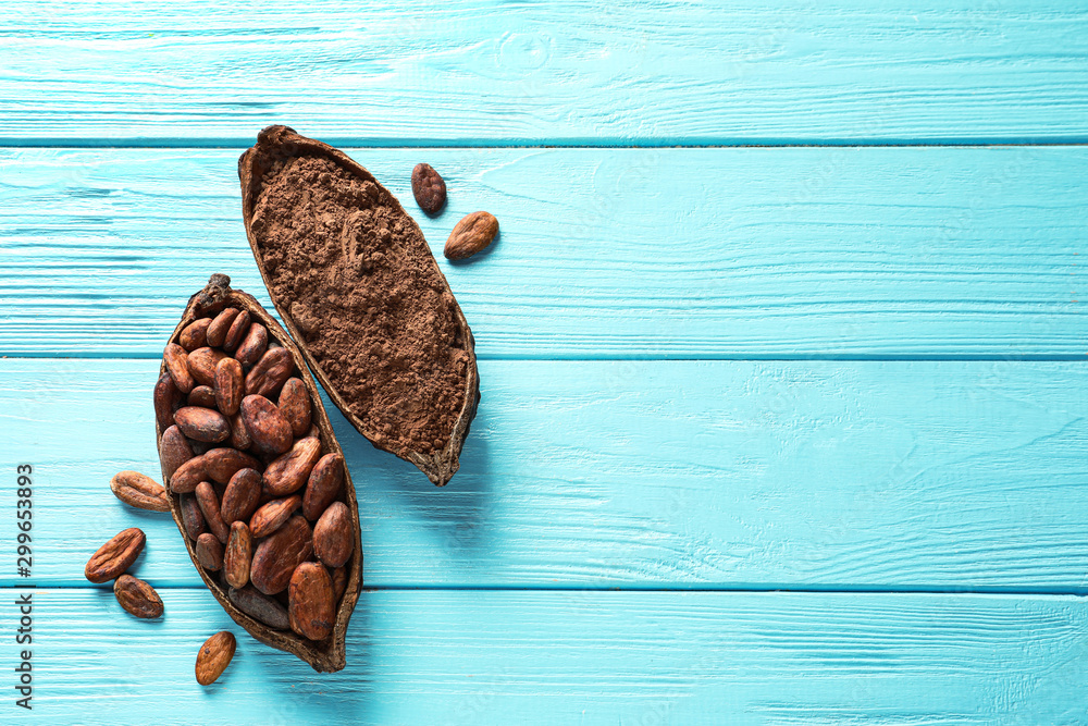 Halves of cocoa pod with beans and powder on blue wooden table, top view. Space for text - obrazy, fototapety, plakaty 