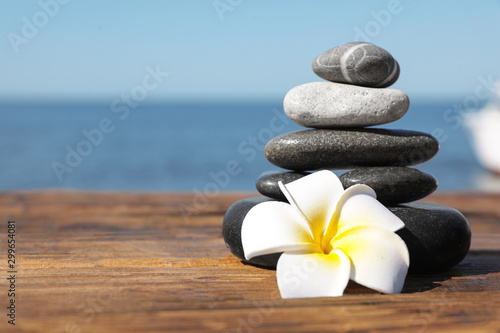 Canvas Print Stack of stones and flower on wooden pier near sea, space for text