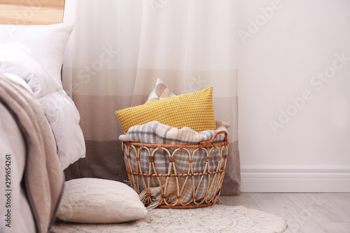 Basket with blanket and pillows near bed indoors