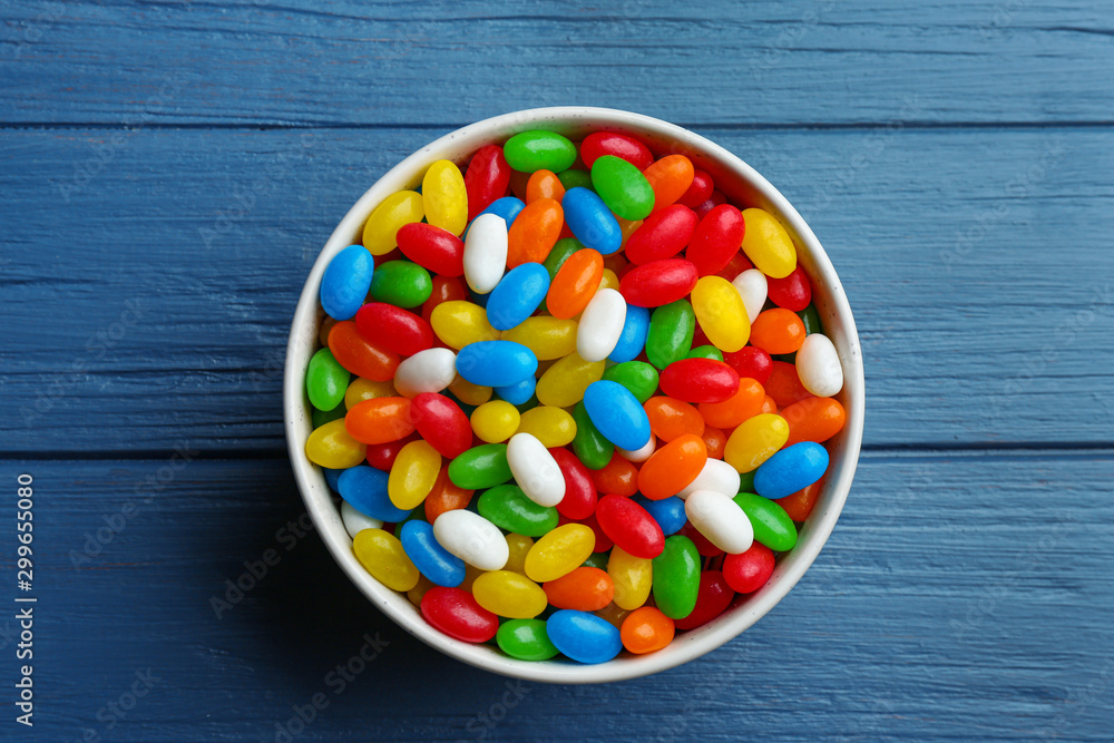 Bowl with colorful jelly beans on blue wooden background, top view