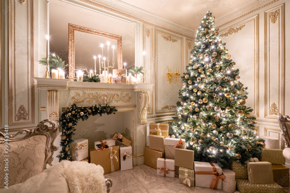 Christmas evening in the light of candles and garlands. Classic luxurious apartments with decorated christmas tree and presents. Living with fireplace, columns and stucco. Christmas evening in the light of candles and garlands. Classic luxurious apartments with decorated christmas tree and presents. Living with fireplace, columns and stucco.