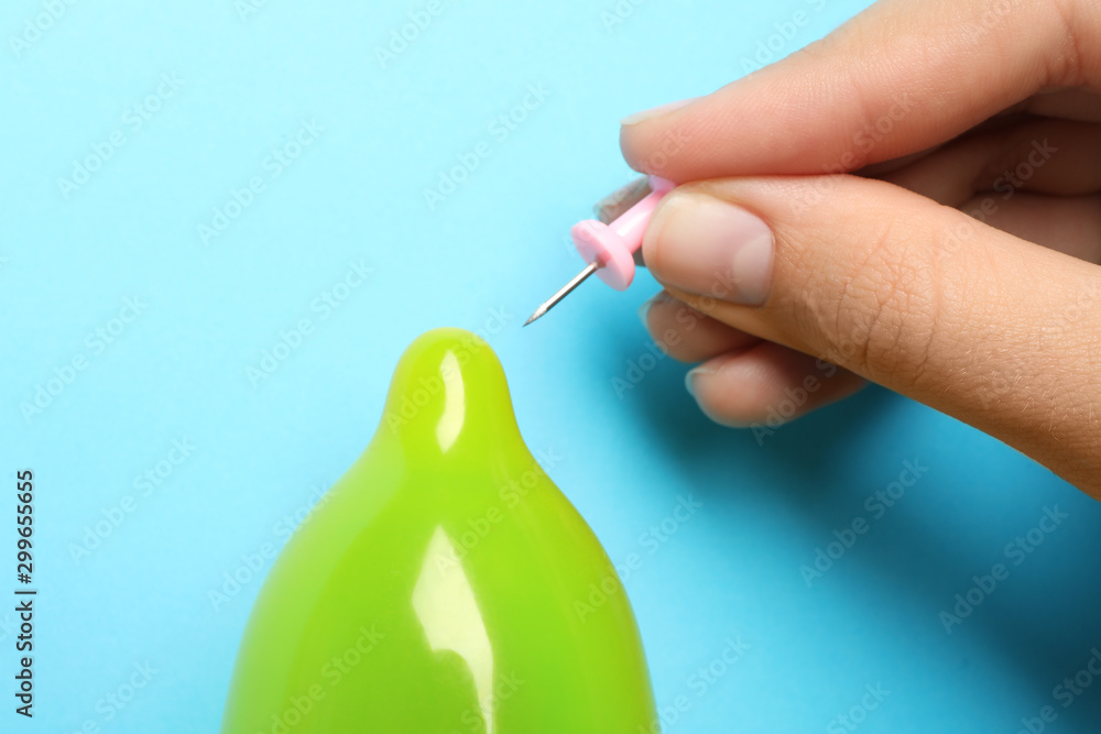 Woman piercing inflated condom with pin on light blue background, closeup. Safe sex Woman piercing inflated condom with pin on light blue background, closeup. Safe sex
