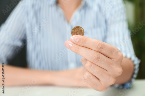 Woman holding coin at light table indoors, closeup