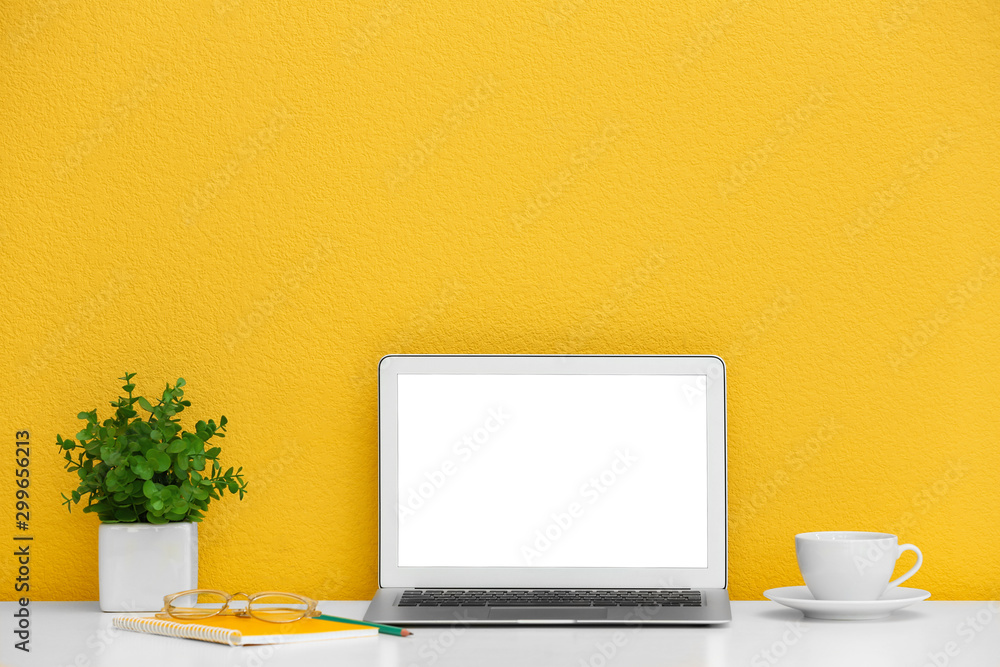 Modern laptop on desk near yellow wall, space for design. Home workplace - obrazy, fototapety, plakaty 