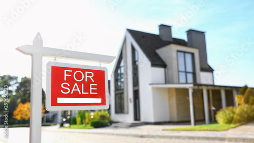 Red real estate sign near house outdoors on sunny day photo