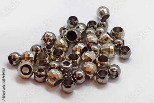 Tips on a cord for a hood or sportswear. Silver-colored plastic fittings in the shape of a ball with two holes. A lot of beads for the cord on a white background.