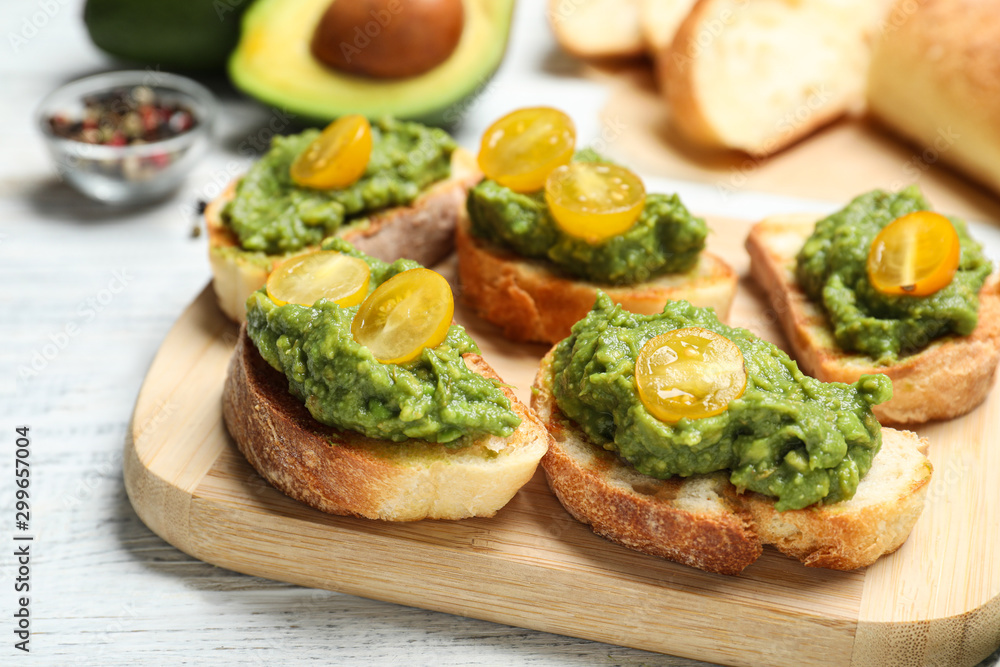 Tasty bruschettas with avocado and yellow cherry tomatoes on white wooden table, closeup