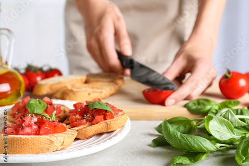 Fototapeta Naklejka Na Ścianę i Meble -  Woman cutting tomato at light grey table, focus on tasty bruschetta