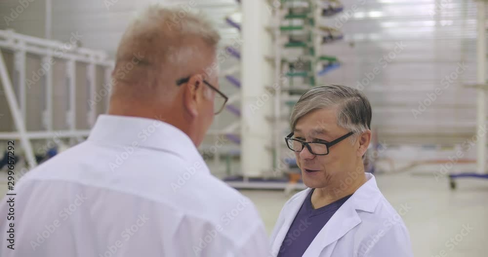 Communication of two satisfied scientists in white coat and glasses talking about results of experiment in innovative high voltage laboratory. Development and creative concept Communication of two satisfied scientists in white coat and glasses talking about results of experiment in innovative high voltage laboratory. Development and creative concept
