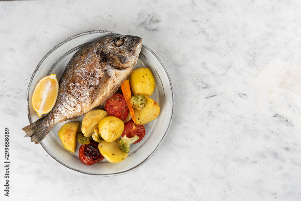 Baked dorado (dorada) fish on a plate, top view